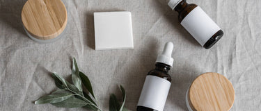 Cremetiegel, Pipettenflaschen mit leeren Etiketten, Seifenstück und Salbeizweig auf Leinen – Pflegeprodukte und ihre Inhaltsstoffe